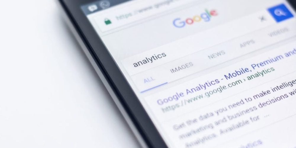 Kuvassa älypuhelin ja Google-haku, jonka tuloksena on Google analytics.